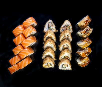 set of Japanese sushi rolls on a black background top view.