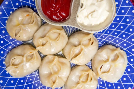 manti and sauce on a blue plate on a burgundy background