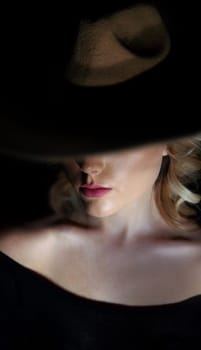 dark studio portrait of an elegant woman in a hat with hidden eyes