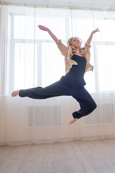 Caucasian woman dances contemporary in ballet class. Dancer in a jump. Vertical photo