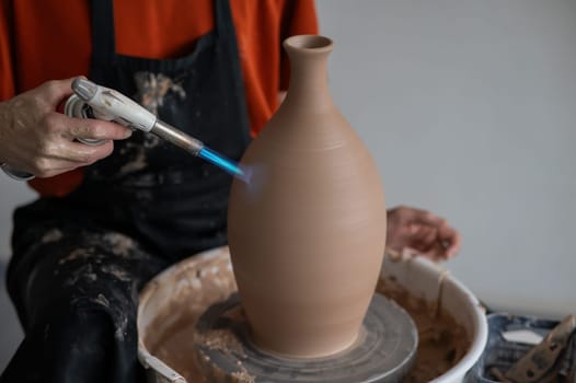 Close-up of a potter's hands firing a jug with a gas burner on a potter's wheel