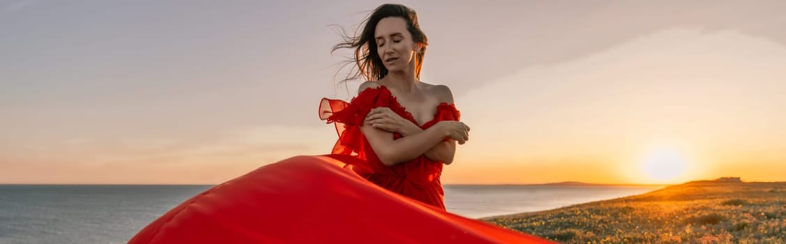 woman red dress standing grassy hillside. The sun is setting in the background, casting a warm glow over the scene. The woman is enjoying the beautiful view and the peaceful atmosphere