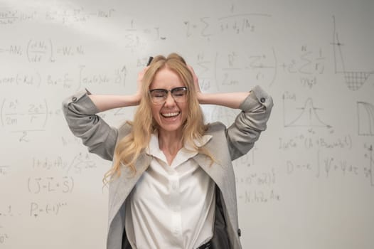 Caucasian woman stands by a white board and holds her head