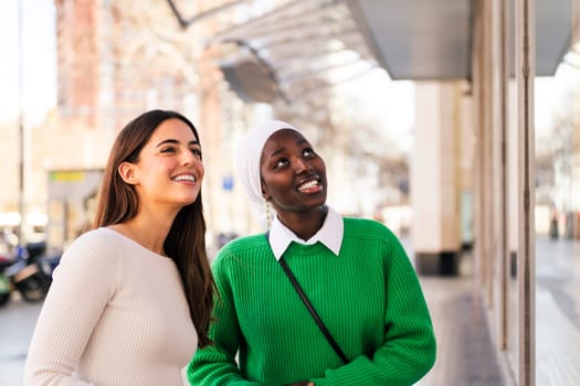 two black and white women smiling happy looking at a shop window, friendship and modern lifestyle concept