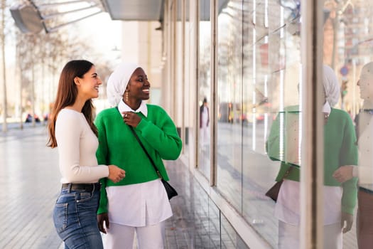 two black and white women smiling happy looking at a shop window, friendship and modern lifestyle concept