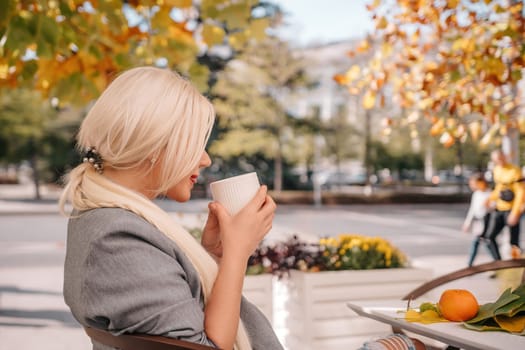 A blonde woman is drinking coffee while sitting under a tree. The scene is peaceful and relaxing, with the woman enjoying her coffee and the natural surroundings