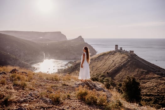 woman stands on a hill overlooking the ocean, her arms raised in the air. Concept of freedom and joy, as if the woman is celebrating a moment of happiness or accomplishment