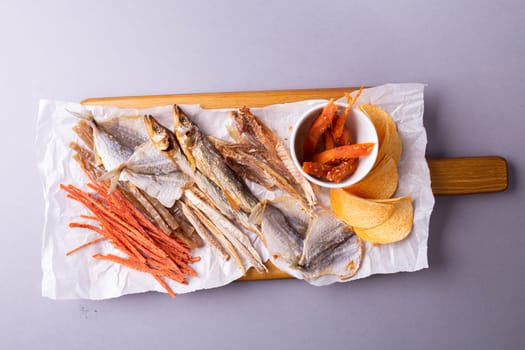 Assorted dried fish, fish skin, and fruit snacks on white paper on a wooden table, creating a vibrant culinary display.