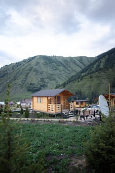 The cozy cabin features a front porch with steps, nestled among lush trees with majestic mountains in the background.