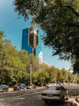 Impressive tall building in blue glass and concrete, surrounded by trees. Modern design and reflection contrast with nature.