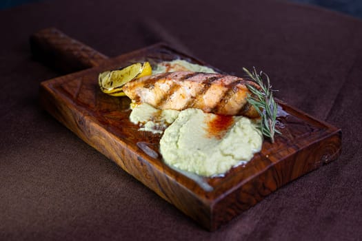 A mouthwatering grilled salmon fillet topped with a zesty lemon-herb butter sauce, presented elegantly on a rustic wooden serving board.