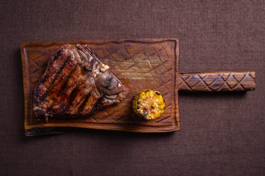 A juicy and tender grilled steak with a side of corn on the cob, served on a rustic wooden cutting board.