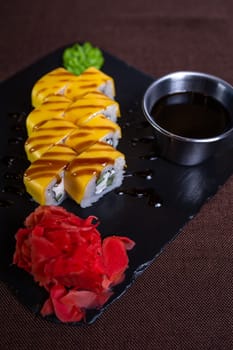 A plate of sushi with cream cheese, cucumber, and eel topped with yellow sauce, wasabi paste, and a flower garnish