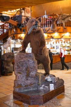 Stuffed brown bear with fish in mouth in cozy lodge with wood walls and fireplace. Wildlife decor theme adds charm to setting.