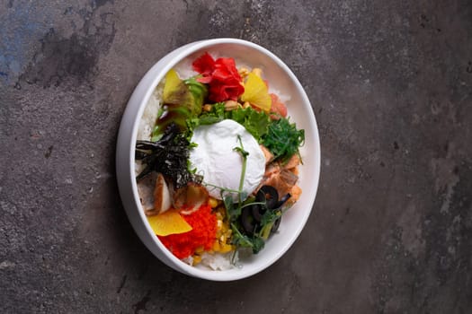 Fresh healthy food ingredients on white plate over dark background. Cucumber, carrot, shrimp, egg, cherry tomatoes, avocado, cabbage, rice.