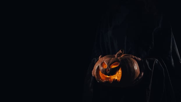 The witch is holding a pumpkin jack o lantern glowing in the dark. Halloween