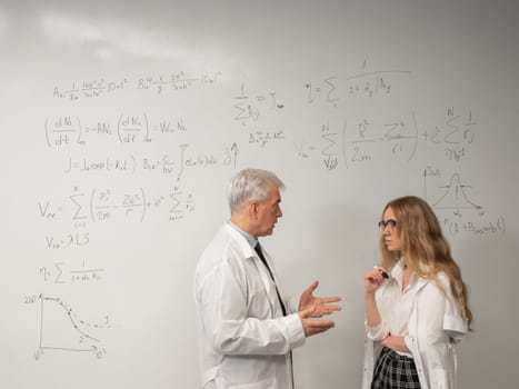 An elderly man and a young woman at a white board. Colleagues scientists discuss work issues