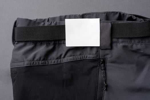 Cardboard label attached to the waistband of dark gray outdoor trousers