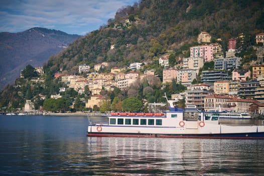 Beautiful touristic boat floating on a clean transparent water of the lake of Como in Italy, against beautiful alpine mountains background. Travel destinations. Tourism. Trip. Famous places concept