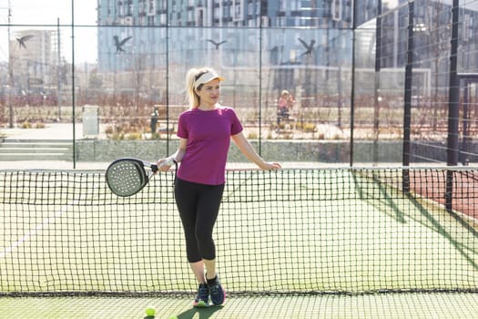 Active young woman trying to beat the ball by Padel racket while playing tennis in the court. High quality photo