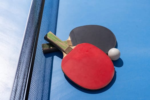 Two table tennis or ping pong rackets and ball on blue table with net. High quality photo