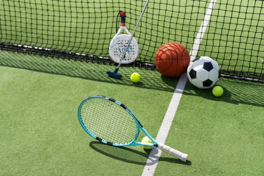 A variety of sports equipment including an american football, a soccer ball, a tennis racket, a tennis ball, and a basketball. High quality photo
