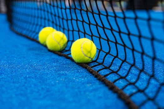 several balls by the net on a blue paddle tennis court. High quality photo