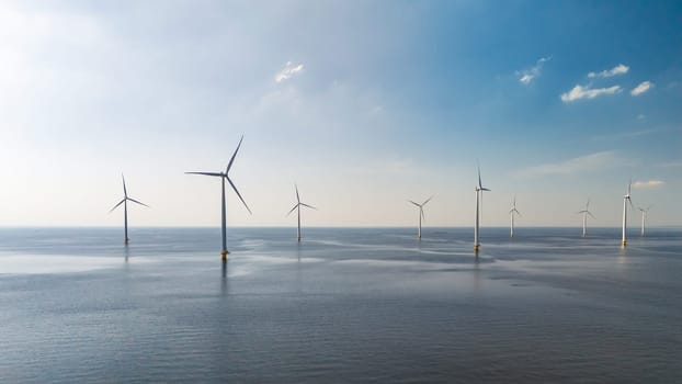 A cluster of windmills gracefully turning their blades against the backdrop of the vast ocean on a sunny day in Flevoland, the Netherlands. Windmill turbines at sea, green energy transition in Europe