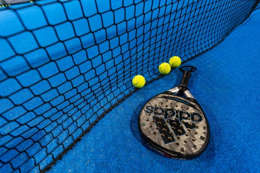 Kyiv, Ukraine, April 18, 2024. Black professional paddle tennis racket and ball with natural lighting on blue background. Horizontal sport theme poster, greeting cards, headers, website and app. High quality photo