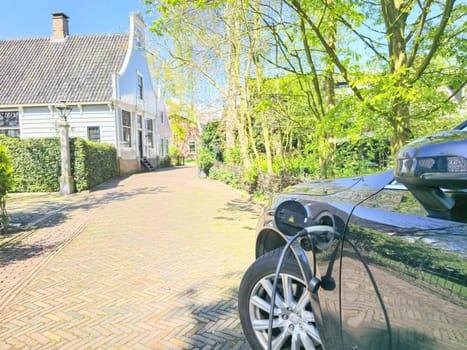 An electric EV car, shining under the sun, sits gracefully parked in front of a charming house in a quiet neighborhood in the Netherlands