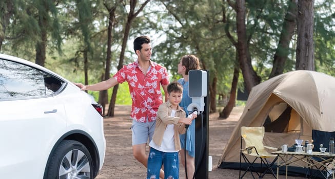 Outdoor adventure and family vacation camping in nature travel by eco friendly car for sustainable future. Lovely family recharge EV car with EV charging station in campsite. Perpetual