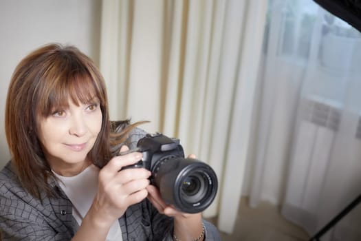 Senior old elderly woman with black camera with a large lens indoors in the studio. Professional photographer. Age Hobby