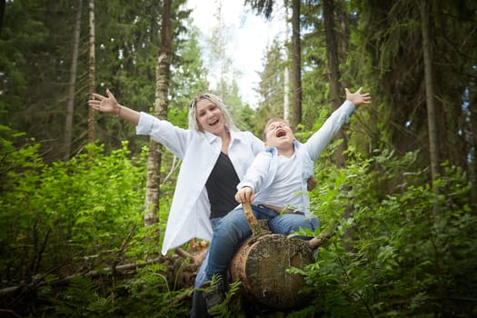 Funny mother with dreadlocks and fat boy happy hugging in forest on a sunny summer day