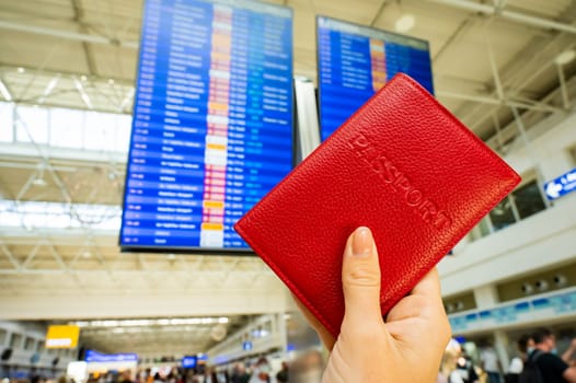 Woman holding a passport against the background of an airport information board