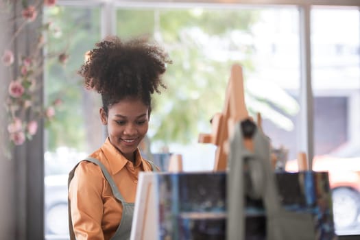 A young black artist paints acrylic paints on canvas with determination in her painting studio.