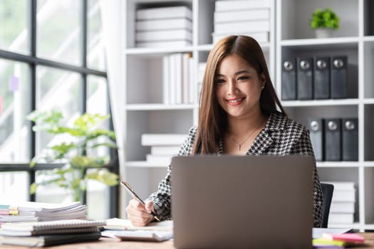 Beautiful accountant sitting working with laptop calculating financial and tax figures for company on desk in living room..