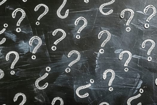 A chalkboard with many questions written on it. The questions are in different sizes and shapes, and some are overlapping. Scene is one of curiosity and learning. Generative AI