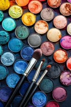 Makeup brushes and colorful eyeshadows on black background. Generative AI.