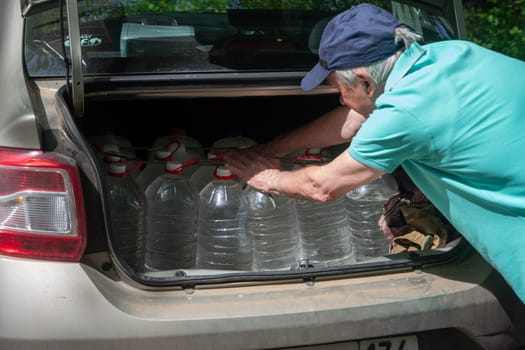 middle aged man loads plastic bottles of spring fresh water into the trunk of a car, free source, High quality photo