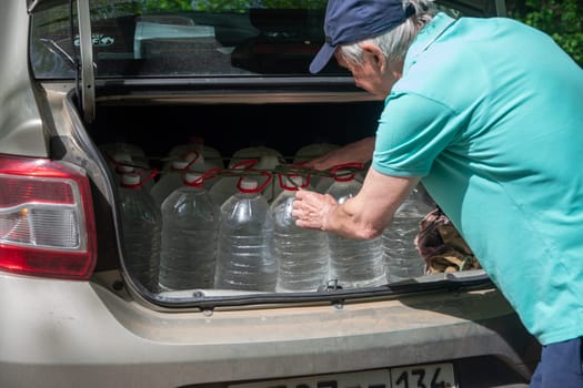 male volunteer loads many five-liter bottles of clean drinking water into the trunk to help victims of a natural disaster. High quality photo