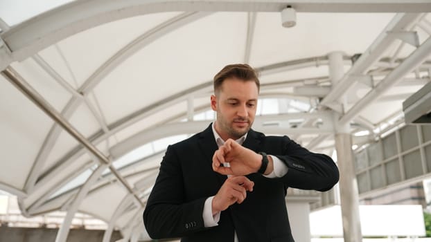 Skilled business man looking watch while walking to train station for going to workplace at bridge. Caucasian manager checking time for important appointment and walk along modern urban city. Urbane.