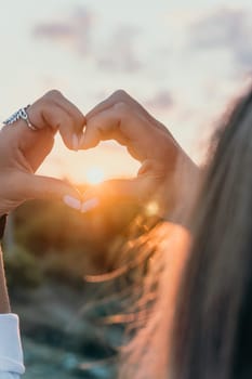 A woman's hand is holding a heart shape, with the sun shining on it. Concept of love and warmth, as the sun symbolizes happiness and positivity. The heart shape represents the bond between two people
