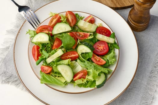 Salad of chopped cherry tomatoes and cucumbers in a white round plate on the table, healthy food. Top view