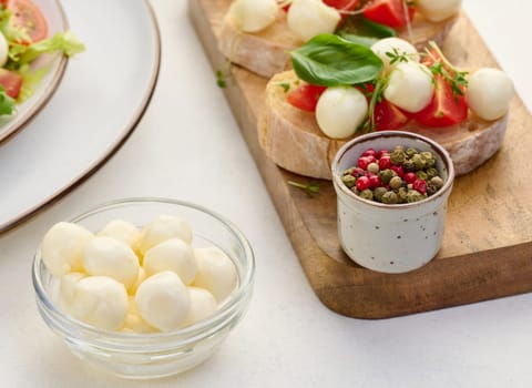 Mozzarella balls in glass bowl and salad on a white background, close up
