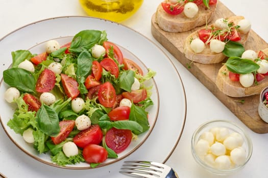 Salad with mozzarella, cherry tomatoes and green lettuce in a white round plate on the table, top view