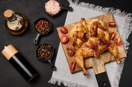 Whole fried chicken with spices on a wooden board on a black table, top view