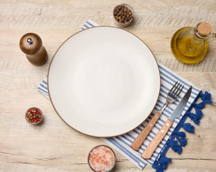 Empty round white plate, olive oil, spices on wooden table, top view