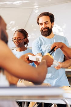 Portrait of a friendly volunteer distributing free food to a crippled homeless person. Detailed image shows a caucasian man helping during a food drive to serve hot meals to the poor and needy.