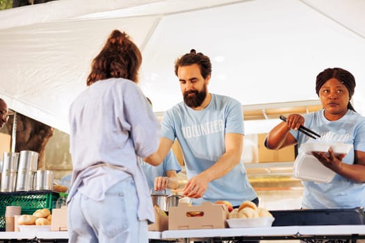 Charitable volunteers distributing free meals to homeless and needy individuals at an outdoor local food bank. Hunger relief team supporting and providing food assistance to the less fortunate.