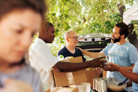 Compassionate group of volunteers providing food to the poor, sharing happiness, and fostering friendship. Outdoor food bank, hunger relief team handing out donation boxes to needy and less fortunate.